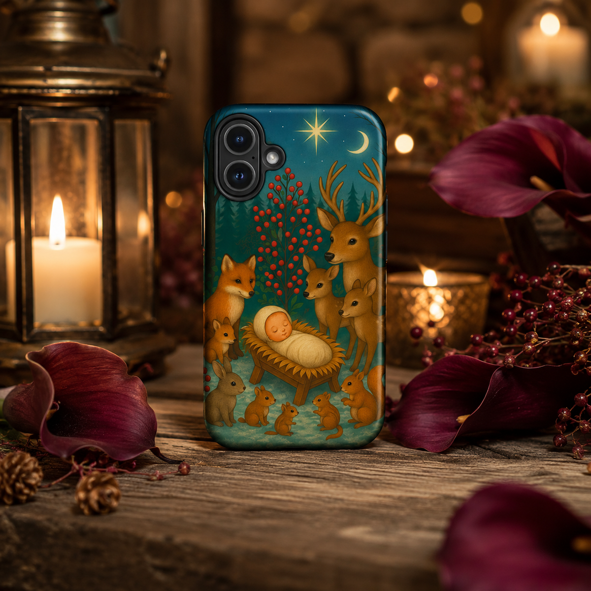 A phone case featuring a Christmas nativity scene with deer, foxes, a baby in a manger, and a star, shown standing on a rustic wooden surface surrounded by candles, lanterns, and dark red flowers.