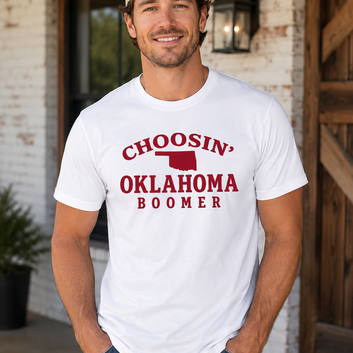 Man wearing a white t-shirt with 'CHOOSIN' OKLAHOMA BOOMER' text and graphic, standing in front of a brick wall.
