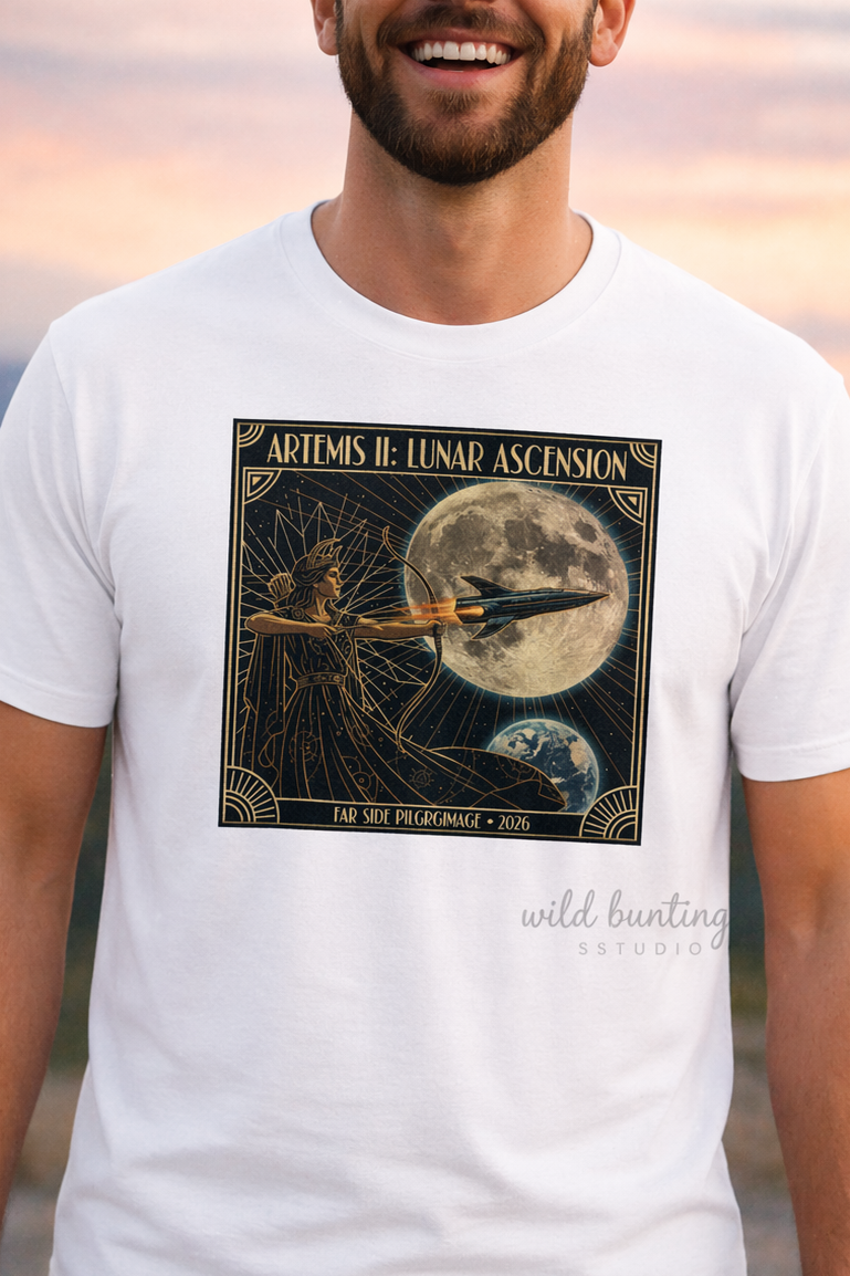 Man wearing a white t-shirt with a graphic design of a rocket and moon, standing against a sunset landscape.