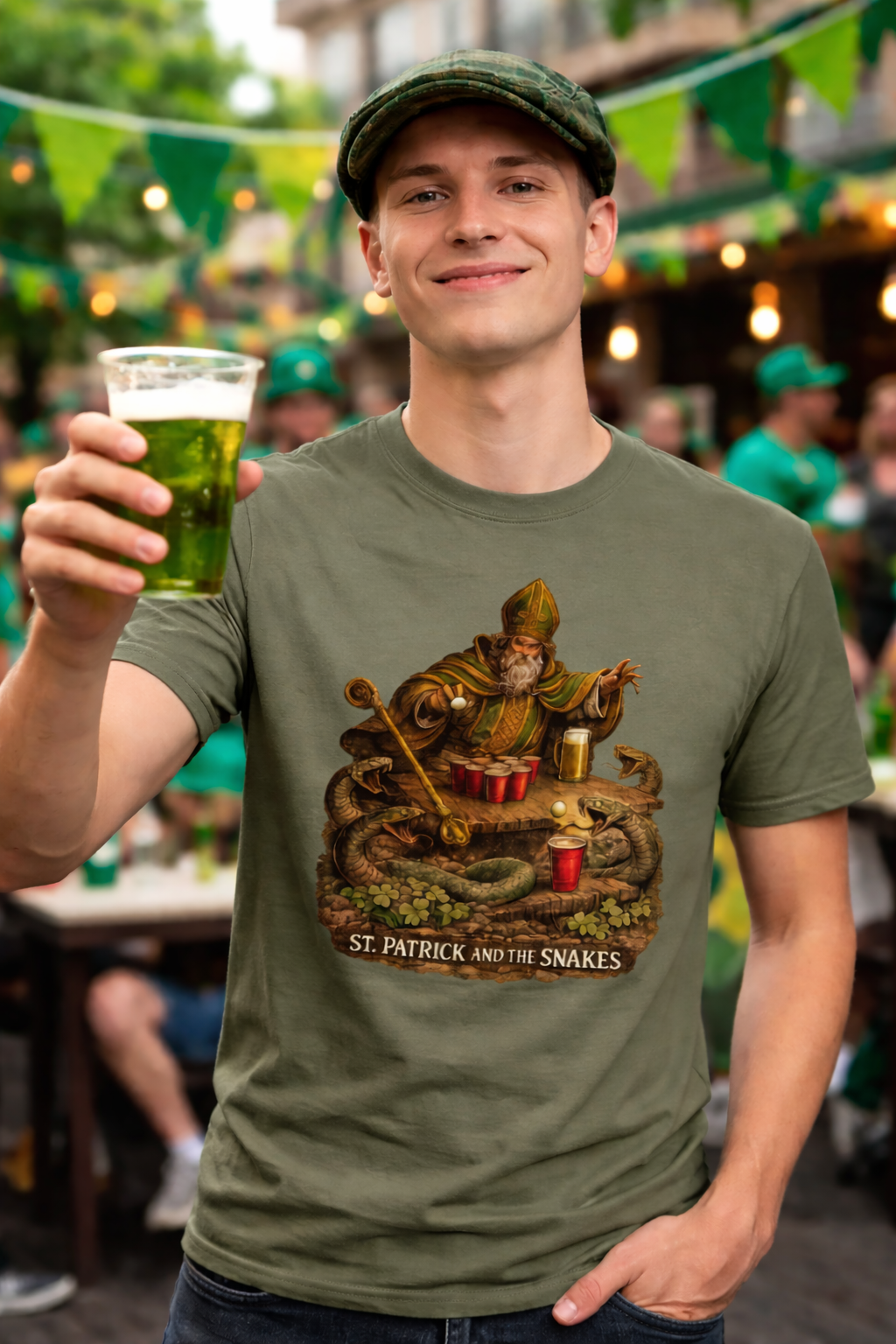 Man wearing a green t-shirt with a graphic design of St. Peter, snakes and beer pong, holding a glass of green beer in an outdoor setting.