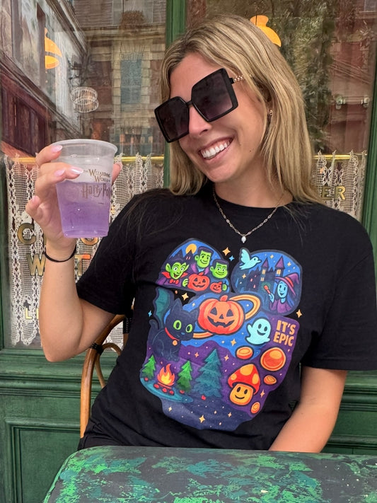 Woman wearing a black t-shirt with colorful Epic Halloween graphic design, holding a purple drink.