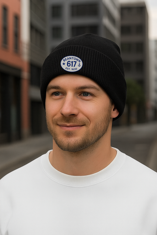 Man wearing a black beanie with a 617 logo and text, standing in an urban setting.