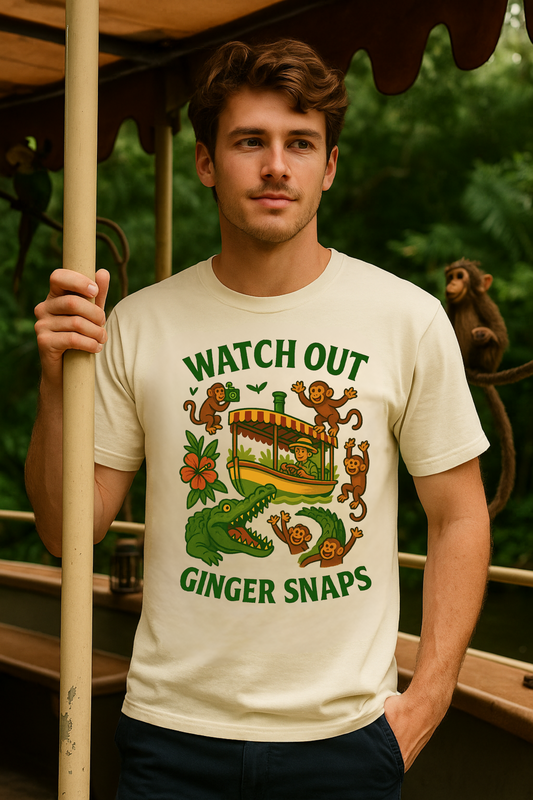 Man wearing a cream-colored graphic tee with a retro jungle cruise design featuring monkeys, a boat, a crocodile, and the text Watch Out Ginger Snaps.