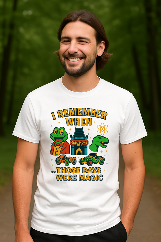 Man wearing a white Gildan 64000 t-shirt with colorful design that says ‘I Remember When Those Days Were Magic,’ featuring a cartoon frog in a suit, a dinosaur, retro ride vehicles, and the Great Movie Ride building.